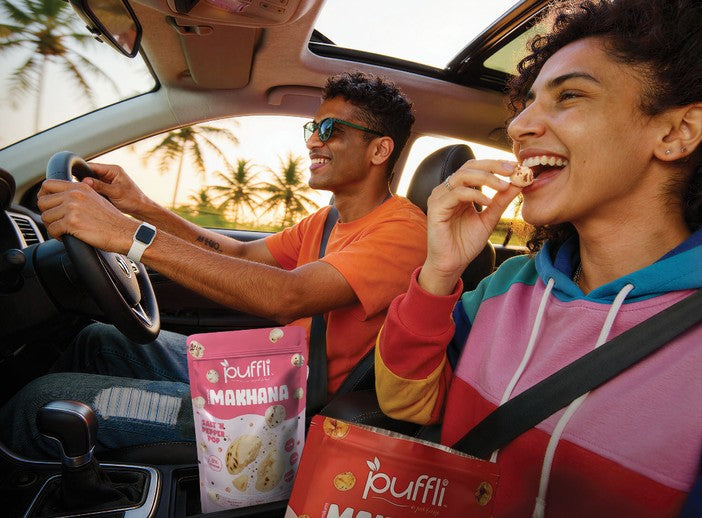 Two friends laughing in a car, snacking on Puffli makhana