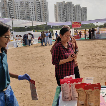 Two women standing outdoors with product packaging, buildings in the background