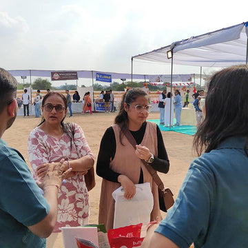 People interacting at an outdoor event with a tent and people in the background.